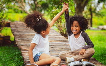 Happy little boy and girl in the park holding hands in the air.