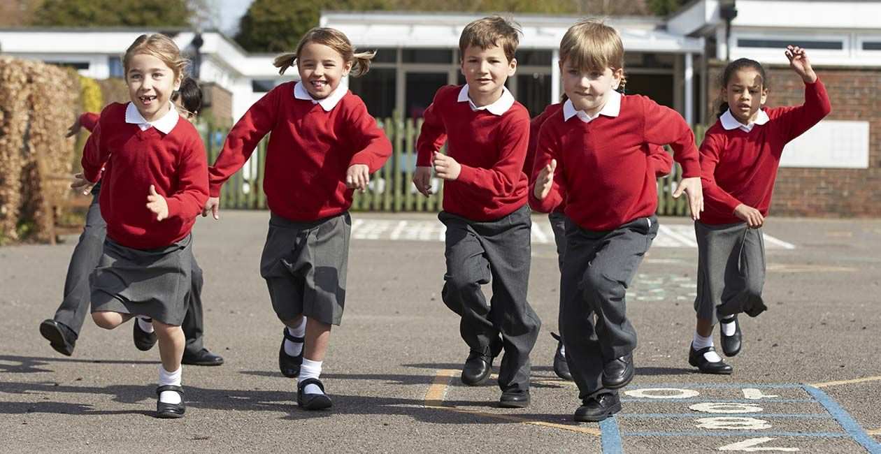 Kids running in the school yard wearing red shirt and grey pant uniforms 