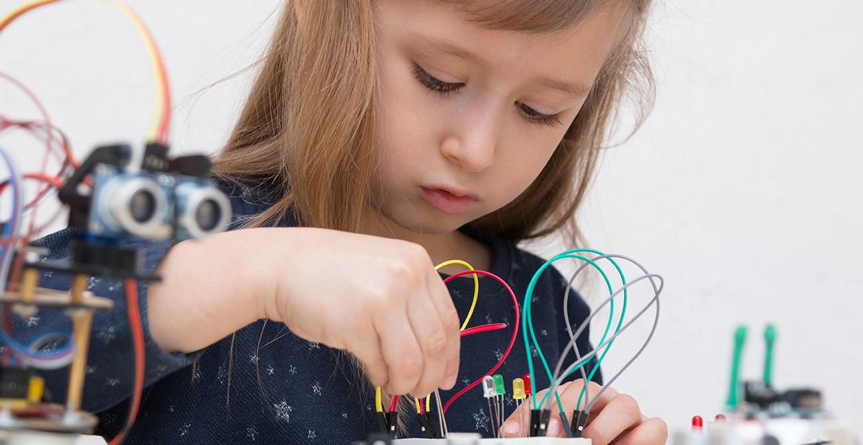 A girl constructs metal robot and program it. The boards and micro controllers are on the table.